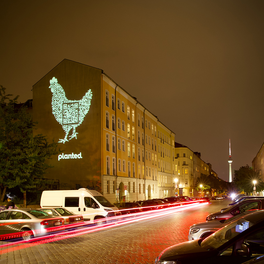 A chicken made of light projected onto a building, with the Berlin TV Tower in the distance